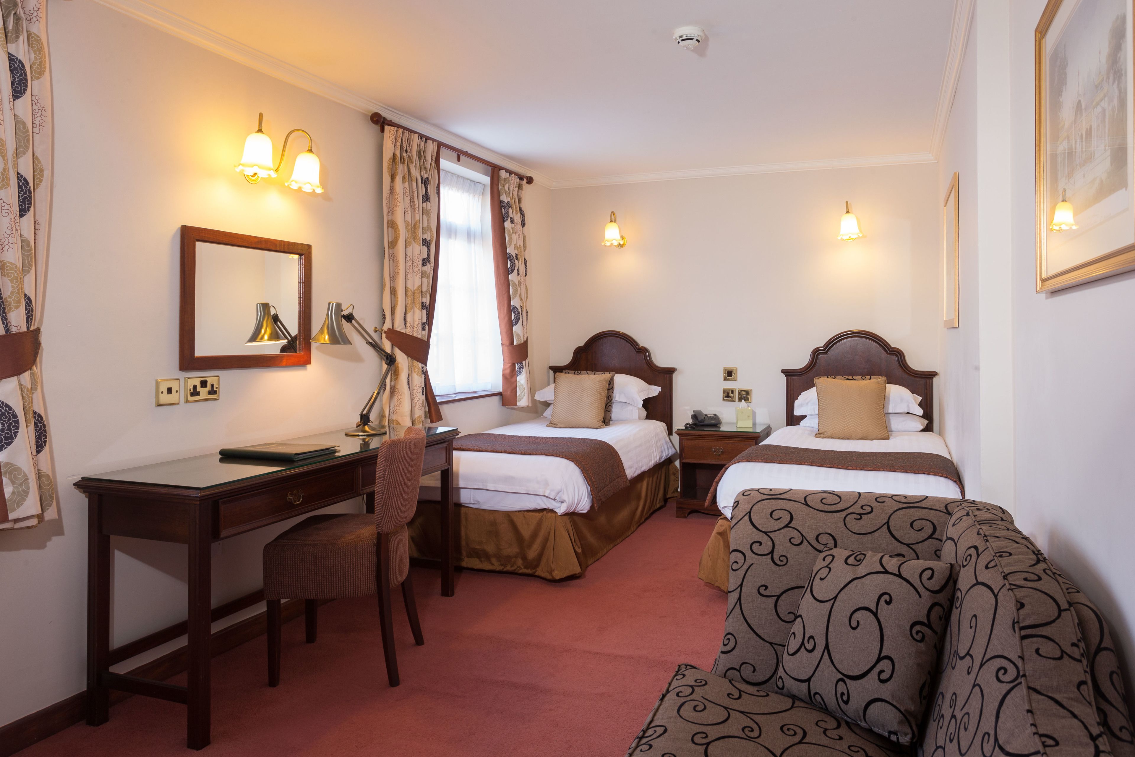 A hotel room with a desk, two beds, a chair, and a sofa.