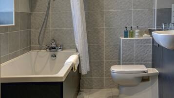 A modern bathroom with a bathtub, toilet, and a small shelf with toiletries.