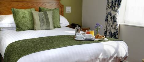 Una cama bien hecha con ropa de cama verde, una bandeja con alimentos para el desayuno y un cabecero de madera.