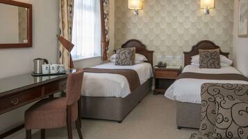 A hotel room with two beds, a desk, a chair, and a lamp.