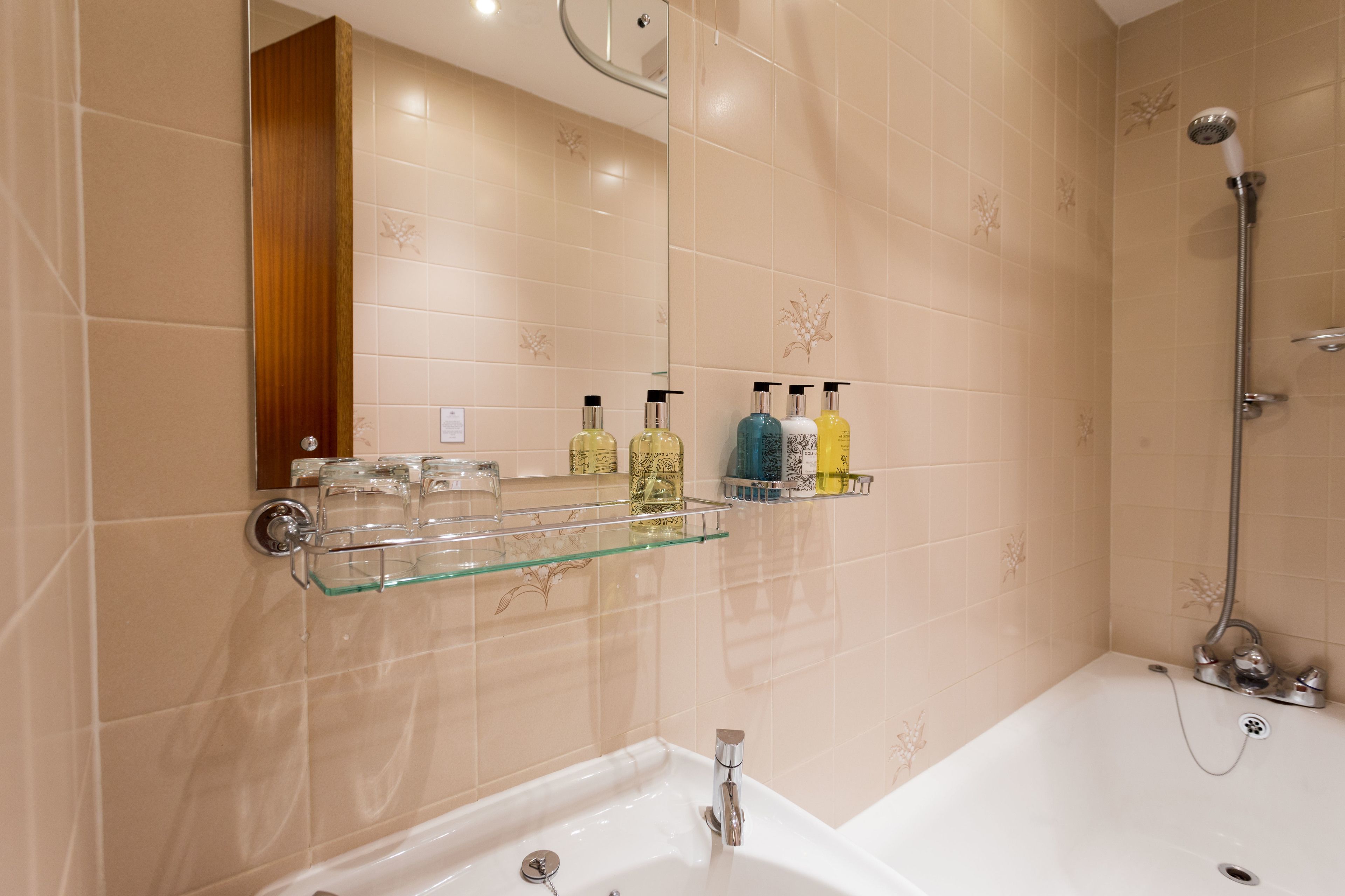 Une salle de bain avec une baignoire, une étagère en verre où sont rangés les articles de toilette et une douche.