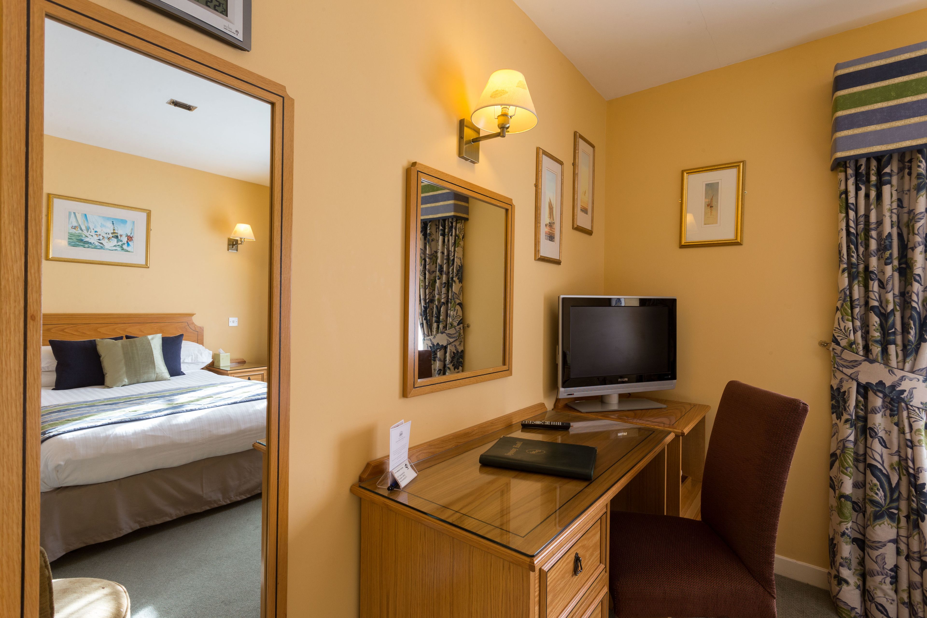 A hotel room with a bed, a desk with a television, a chair, and a mirror.