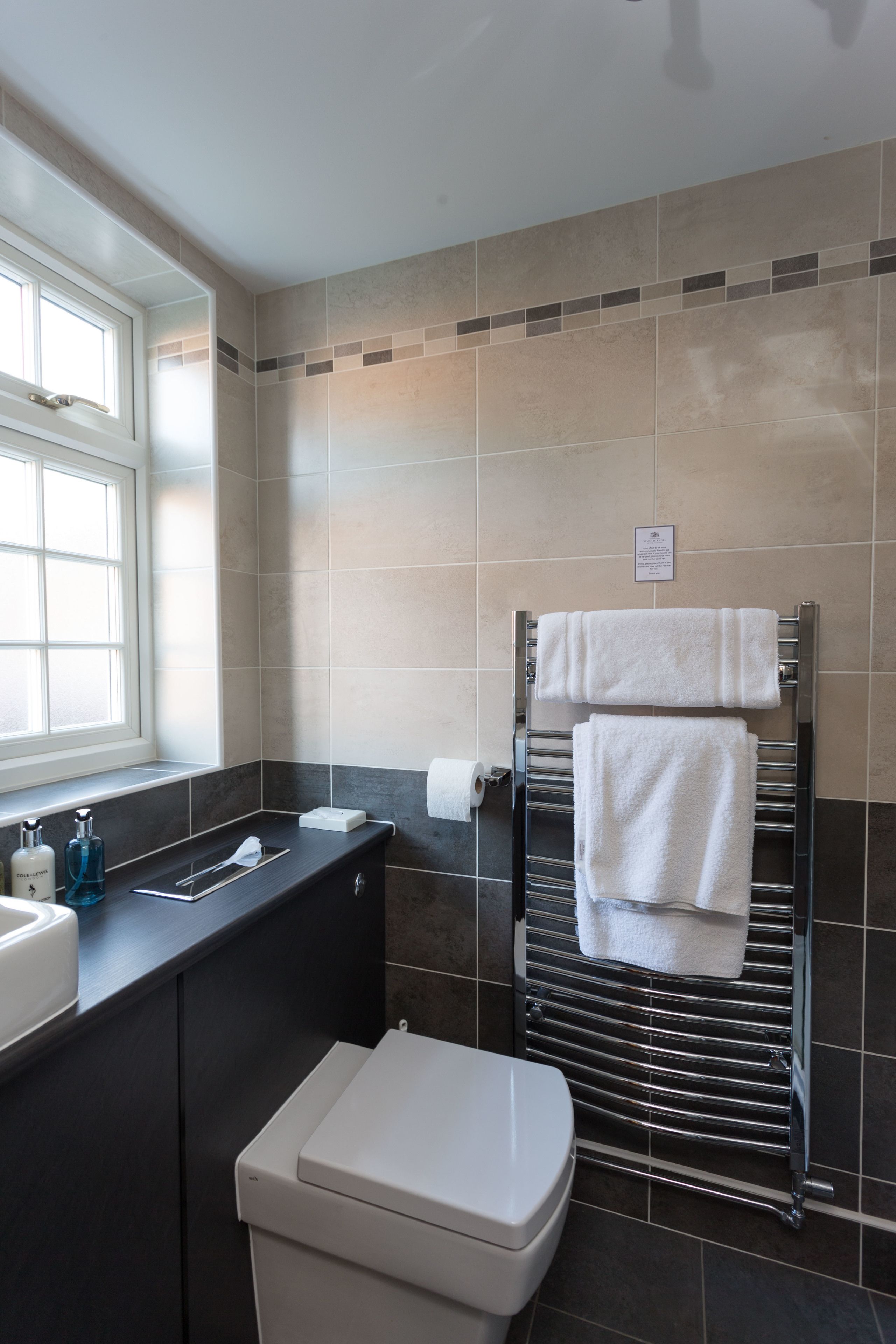 A modern bathroom with a white toilet, a sink with a mirror, and a towel rack with two white towels.
