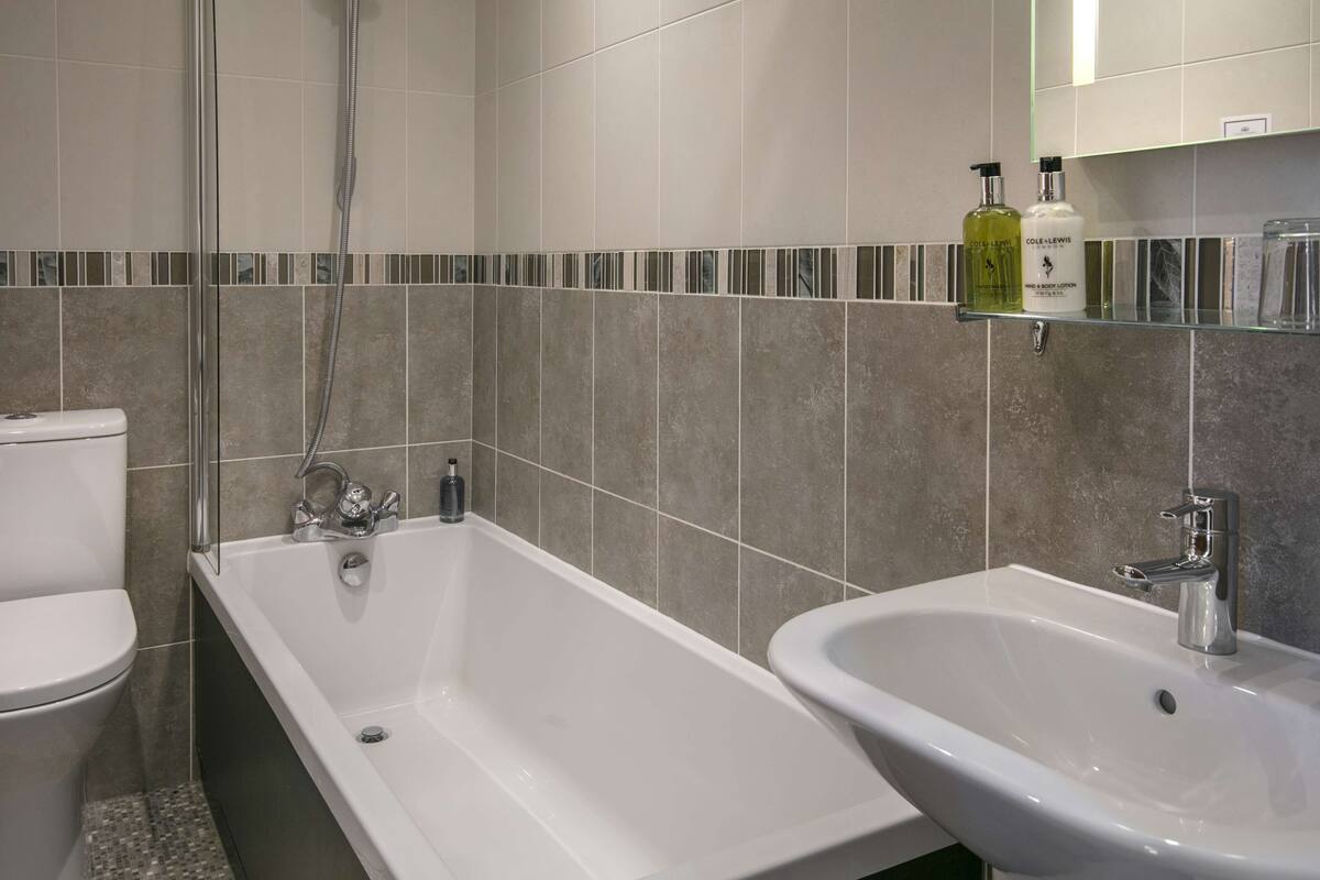 A modern bathroom with a bathtub, a sink, and a toilet. There are two bottles of lotion on a shelf above the sink.