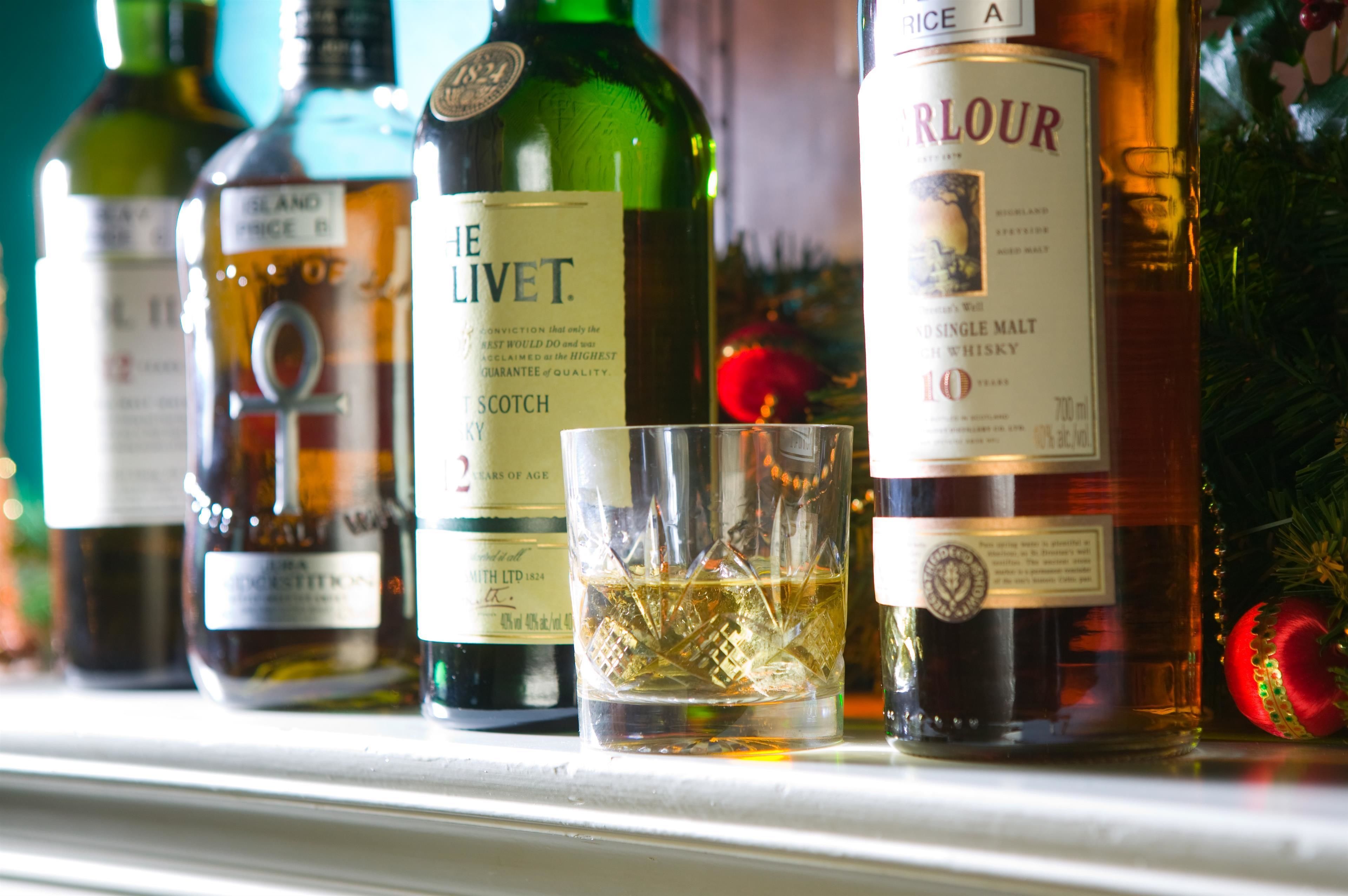 Varias botellas de whisky y un vaso sobre una estantería.