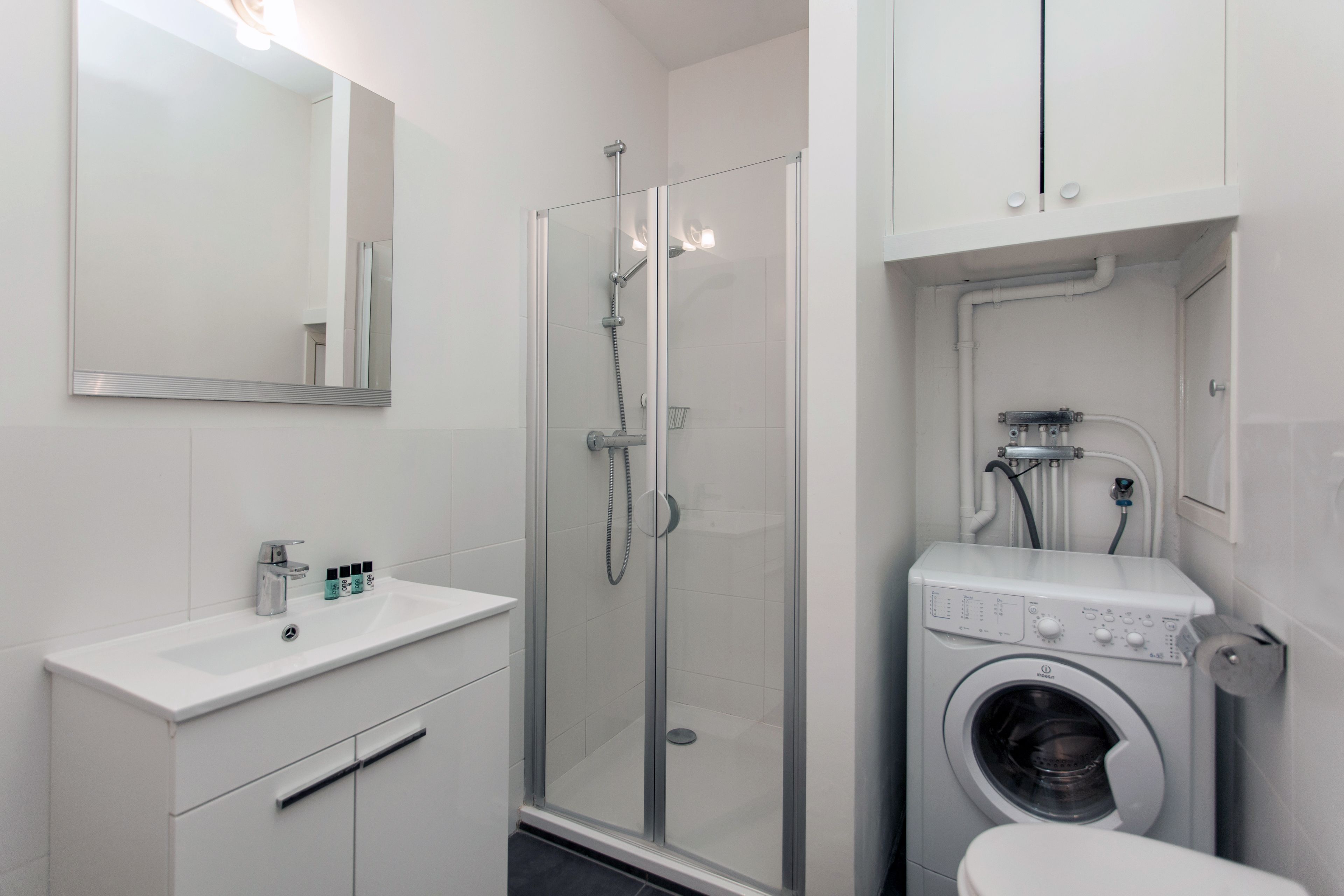 Une salle de bain moderne dotée d’une douche à parois de verre, d’un lave-linge encastré et d’un lavabo blanc avec un miroir au-dessus.
