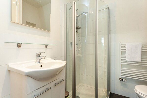 A modern bathroom with a glass-enclosed shower, a white sink, and a toilet. - Stayci Apartments Central Station (The Hague)