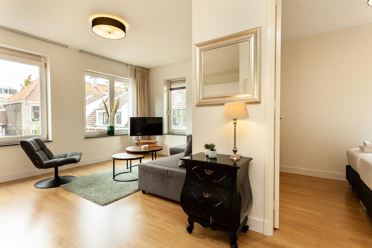 Een moderne hotelkamer met een groot bed, een bureau met een televisie, een comfortabele fauteuil en een grote spiegel.