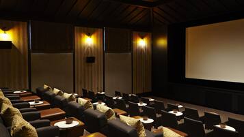A cinema with rows of black leather seats, wooden tables with bowls, and a large screen.