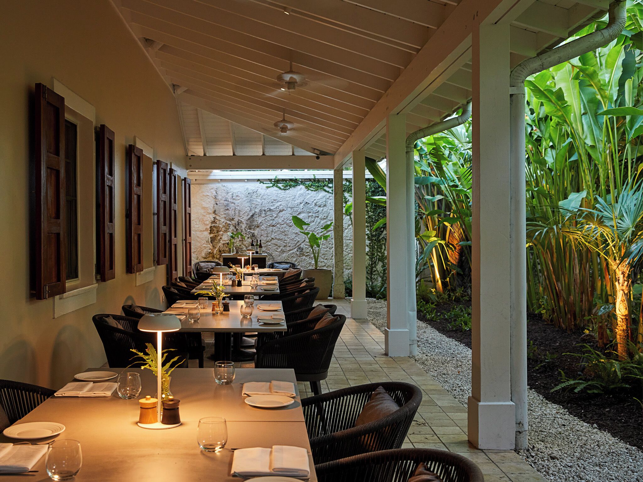 Un espace repas avec une longue table, des chaises et une vue sur des plantes tropicales.