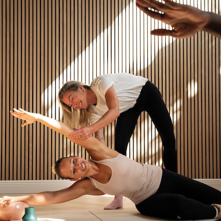 A person performing a stretching exercise on a yoga mat in a room with vertical wooden slats on the wall.