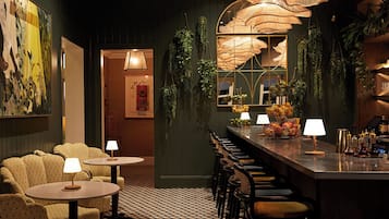 A bar area with a checkered floor, round tables with lamps, and a bar counter with fruit baskets and bottles.