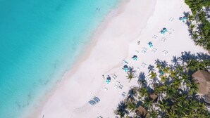 An aerial view of a beach with clear turquoise waters, white sand, and several beach umbrellas and lounge chairs. - The Island House (Nassau)
