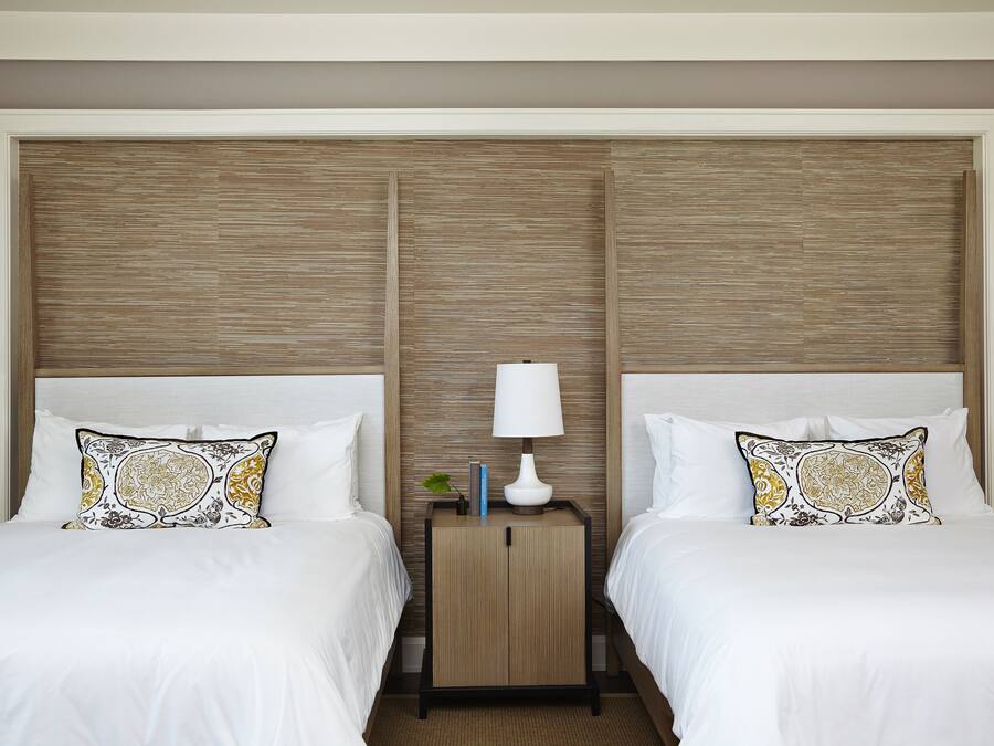 A hotel room with two beds, a nightstand with a lamp, and a decorative pillow.