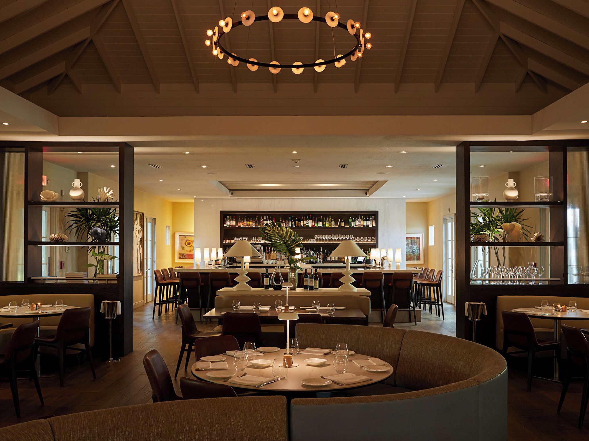 Un restaurant avec des tables rondes, un bar et des étagères remplies de bouteilles et de verres.