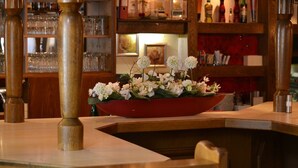 En bardisk med en röd skål fylld med vita blommor placerad på en träbänk, omgiven av trästolar och en bardisk med glas.