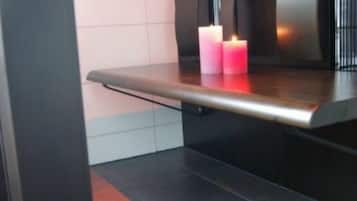 A modern bathroom with a dark countertop, a white tiled wall, and two lit pink candles on the counter.