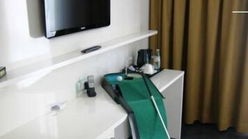 Habitación de hotel con televisor de pantalla plana en la pared, un escritorio con teléfono, mantel verde y taco de billar.