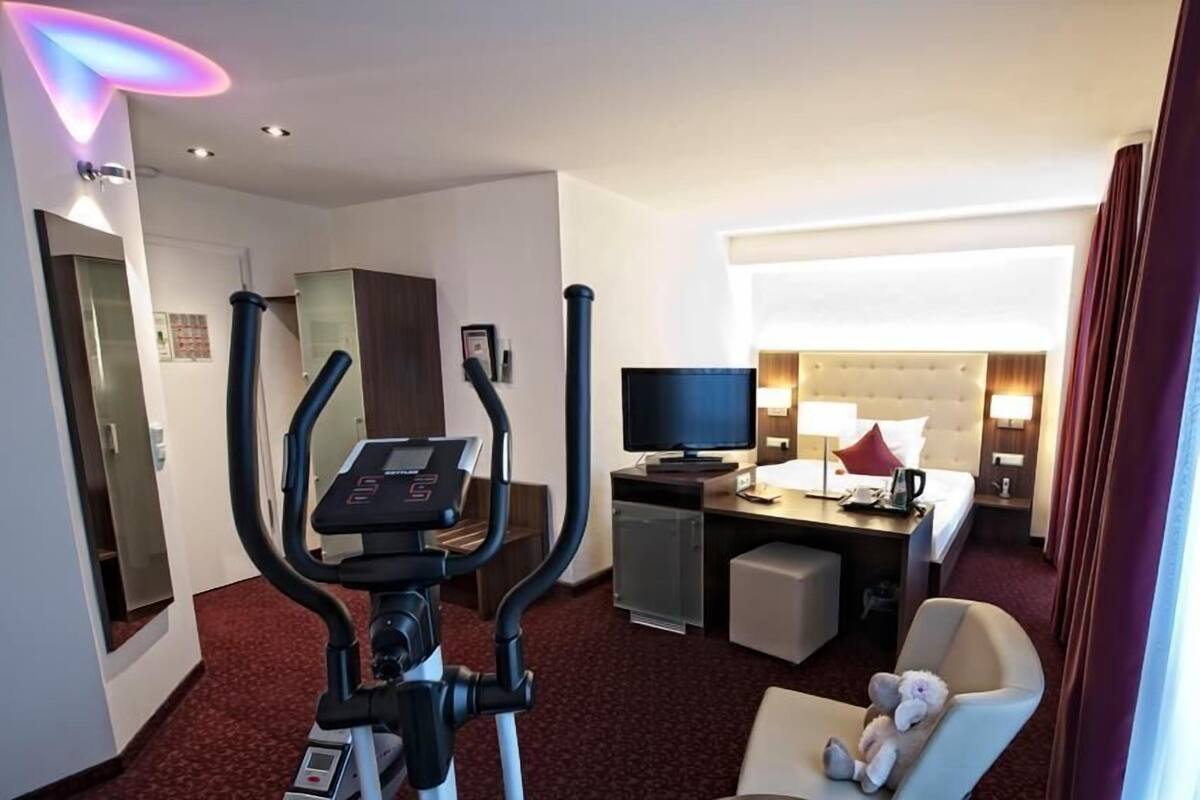 Ein Hotelzimmer mit Laufband, Bett mit Fernseher, Schreibtisch und Stuhl.