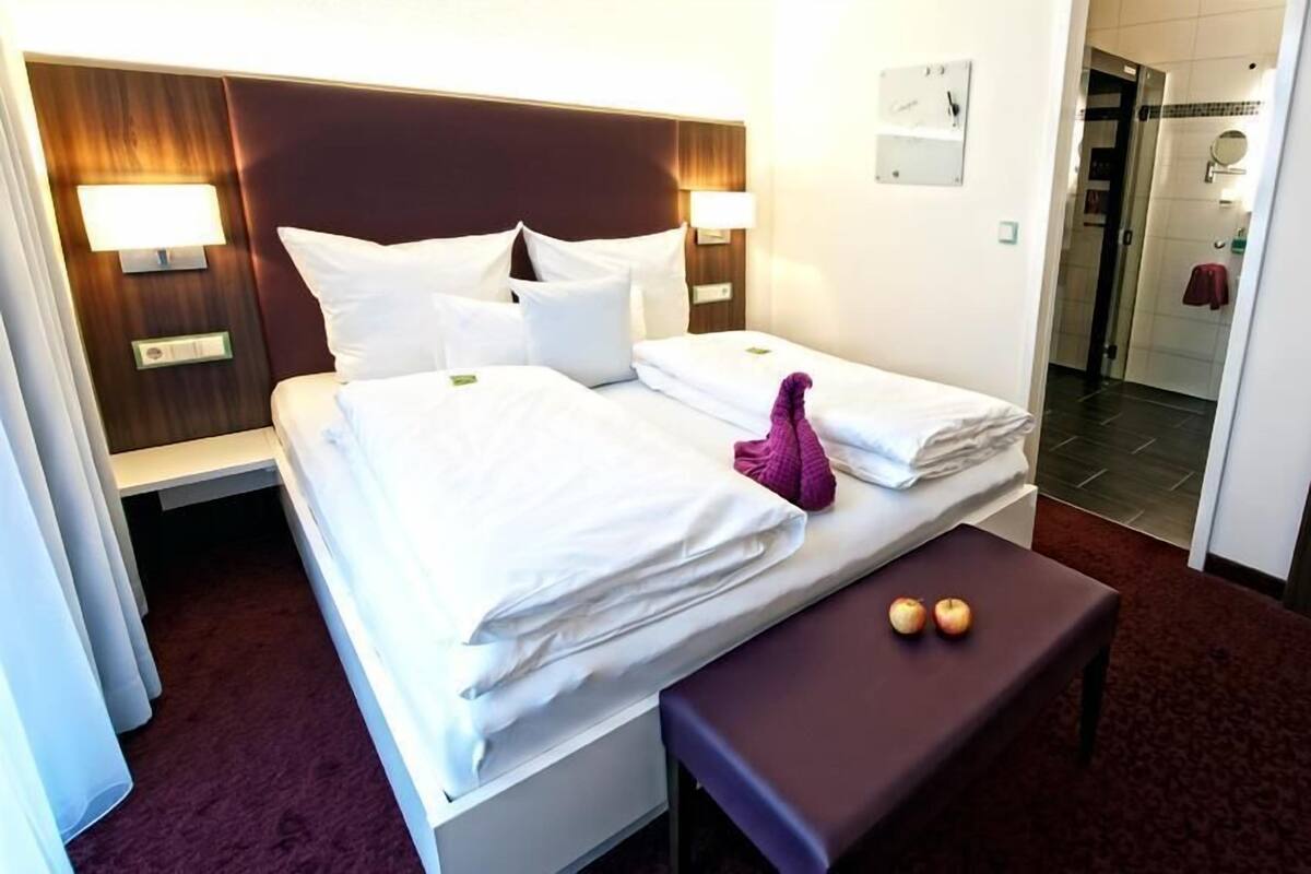 Ein Hotelzimmer mit Doppelbett, zwei Nachttischen, einer Bank und einem kleinen Tisch mit Äpfeln.