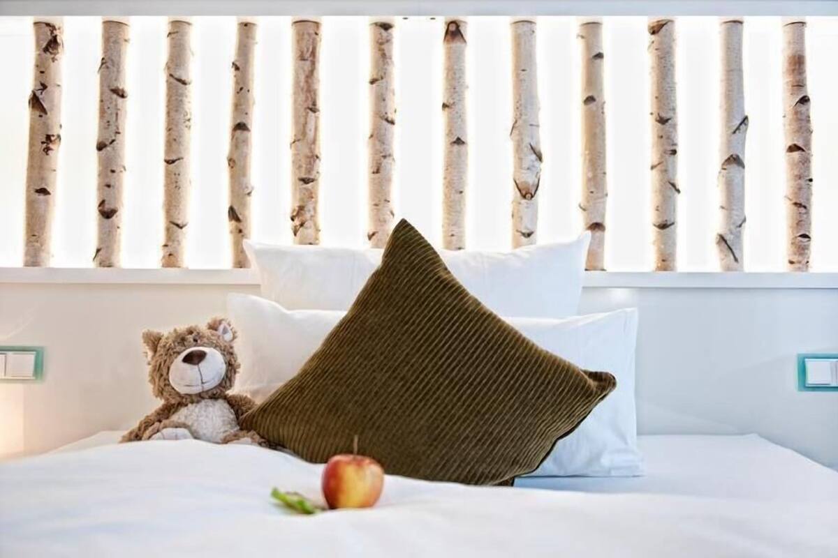 Ein Bett mit einem braunen Kopfkissen, einem Teddybären und einem Apfel auf dem Nachttisch.
