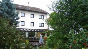 A building with a balcony, surrounded by lush greenery and flowering plants. - Hotel Zum Rosengarten (Darmstadt)