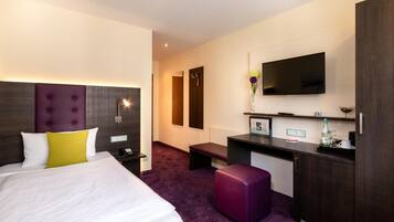 Ein Hotelzimmer mit einem großen Bett, einem Schreibtisch, einem Fernseher und einem violetten Hocker.