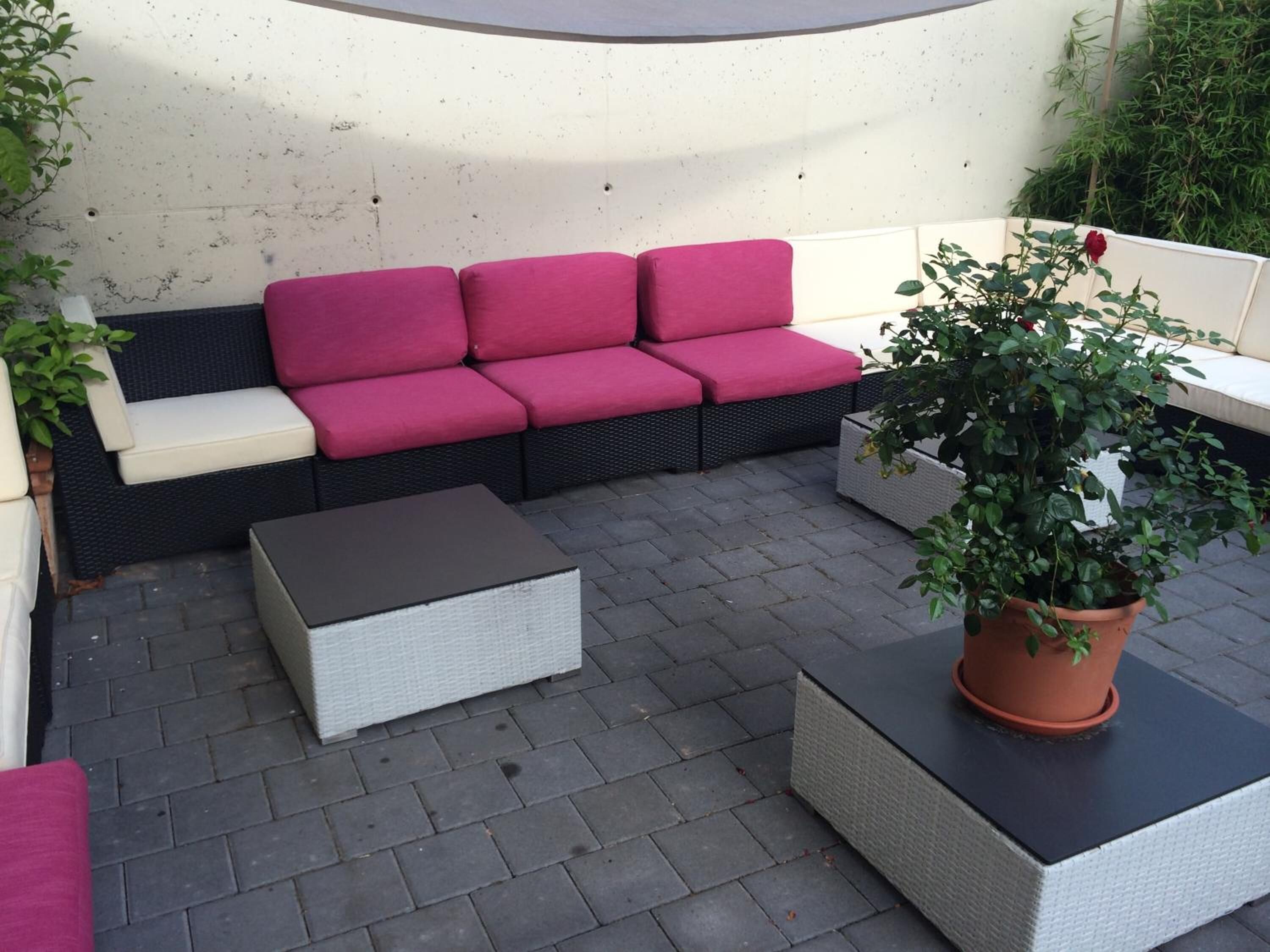 An outdoor seating area with a sofa and two square tables, surrounded by potted plants.