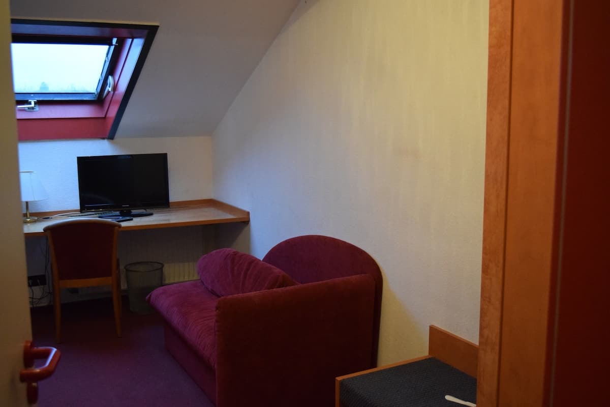 A small room with a sloped ceiling, a desk with a computer, a red chair, and a red sofa.