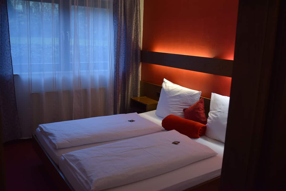 A double bed with white linens, a red pillow, and a wooden headboard.