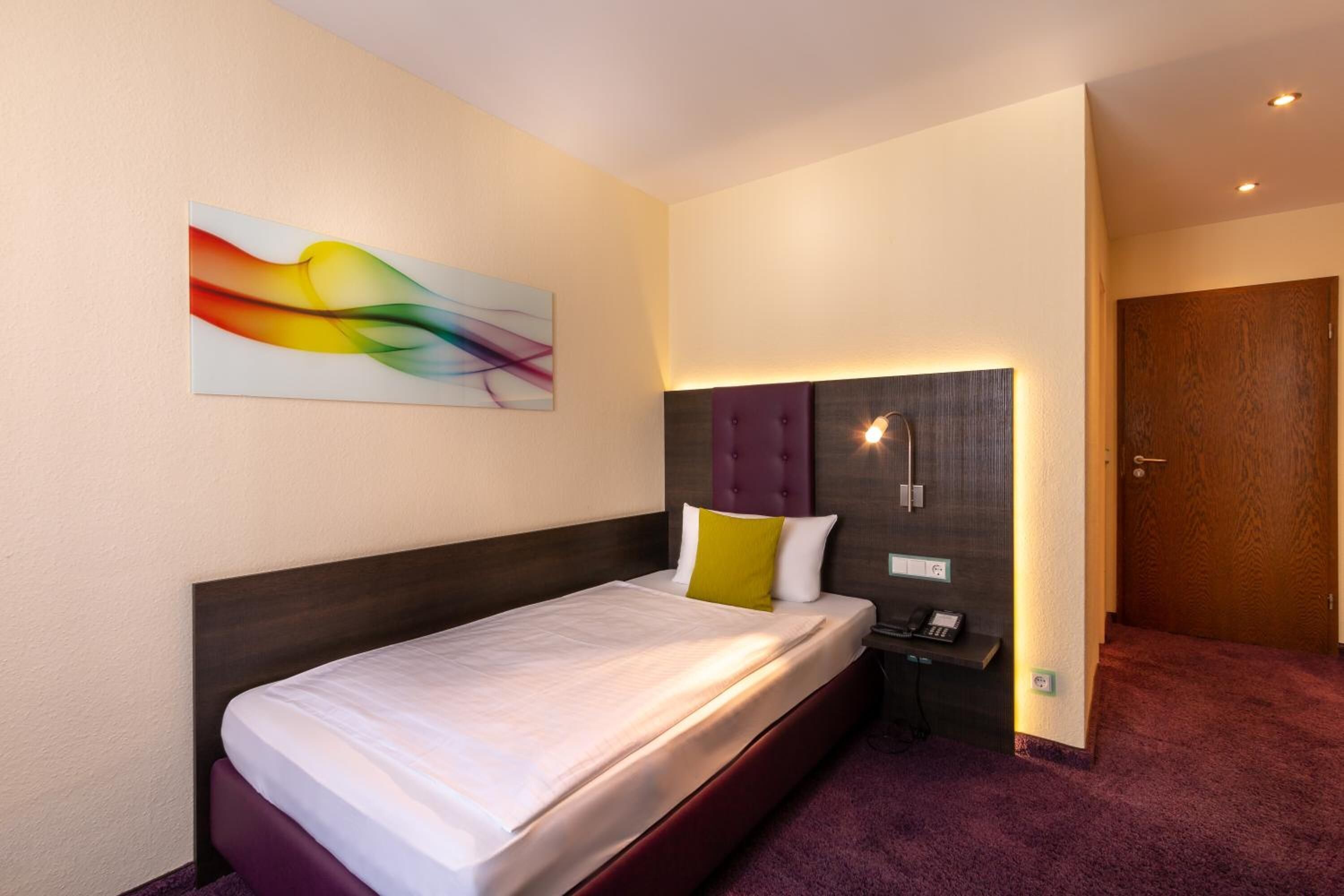 Ein Hotelzimmer mit Bett, Nachttisch, Telefon und Tür.