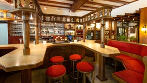 A bar area with wooden beams, a counter, stools, and shelves with bottles and glasses. - Hotel Zum Rosengarten (Darmstadt)