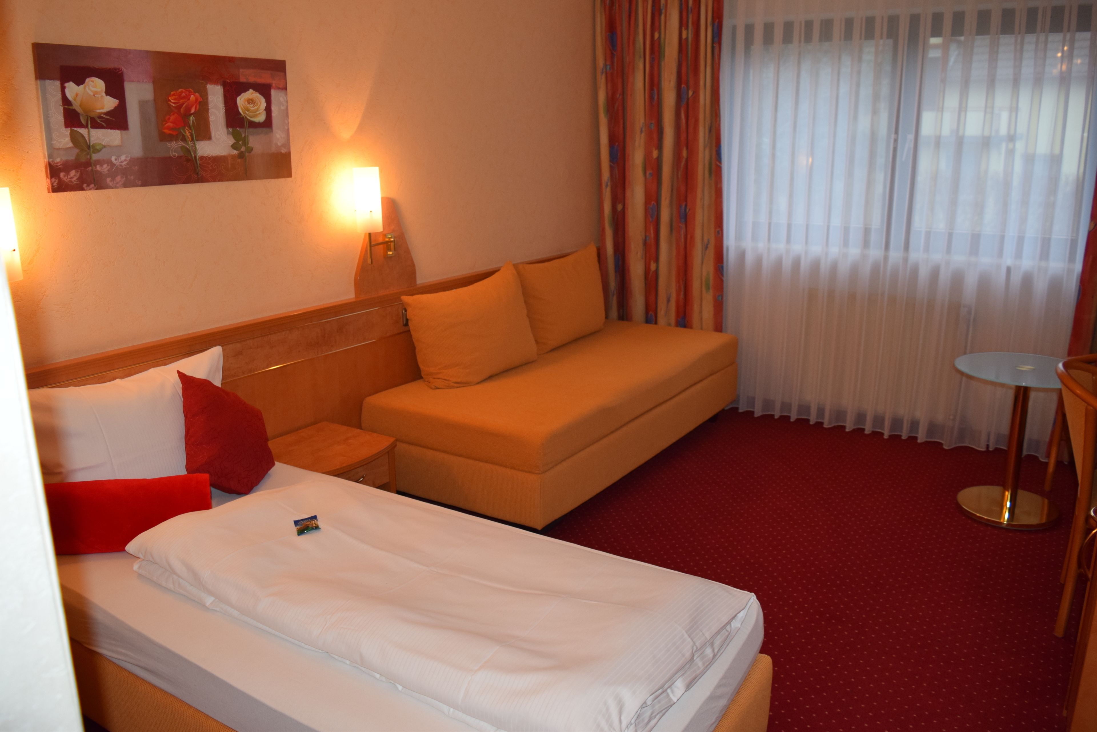A hotel room with a bed, a sofa, a small table, and a painting on the wall.