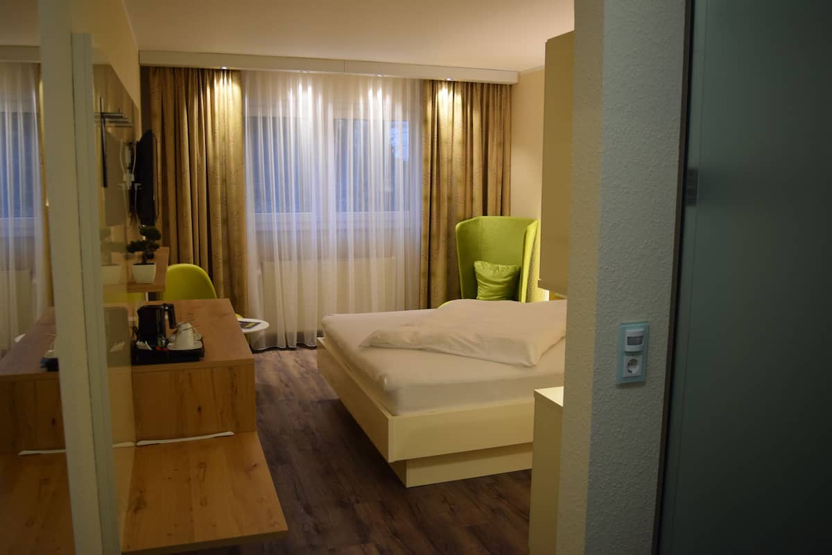 A hotel room with a bed, a desk, a chair, and a large window with curtains.
