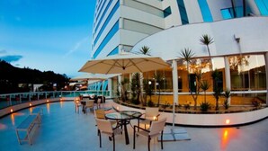Un hotel moderno con área de piscina, mobiliario exterior y fachada de vidrio curvo.