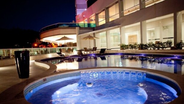 Una piscina con un jacuzzi, sillas de descanso y sombrillas.