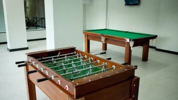 Una mesa de fútbol de mesa y una mesa de billar en una habitación con paredes blancas y suelo de baldosas.