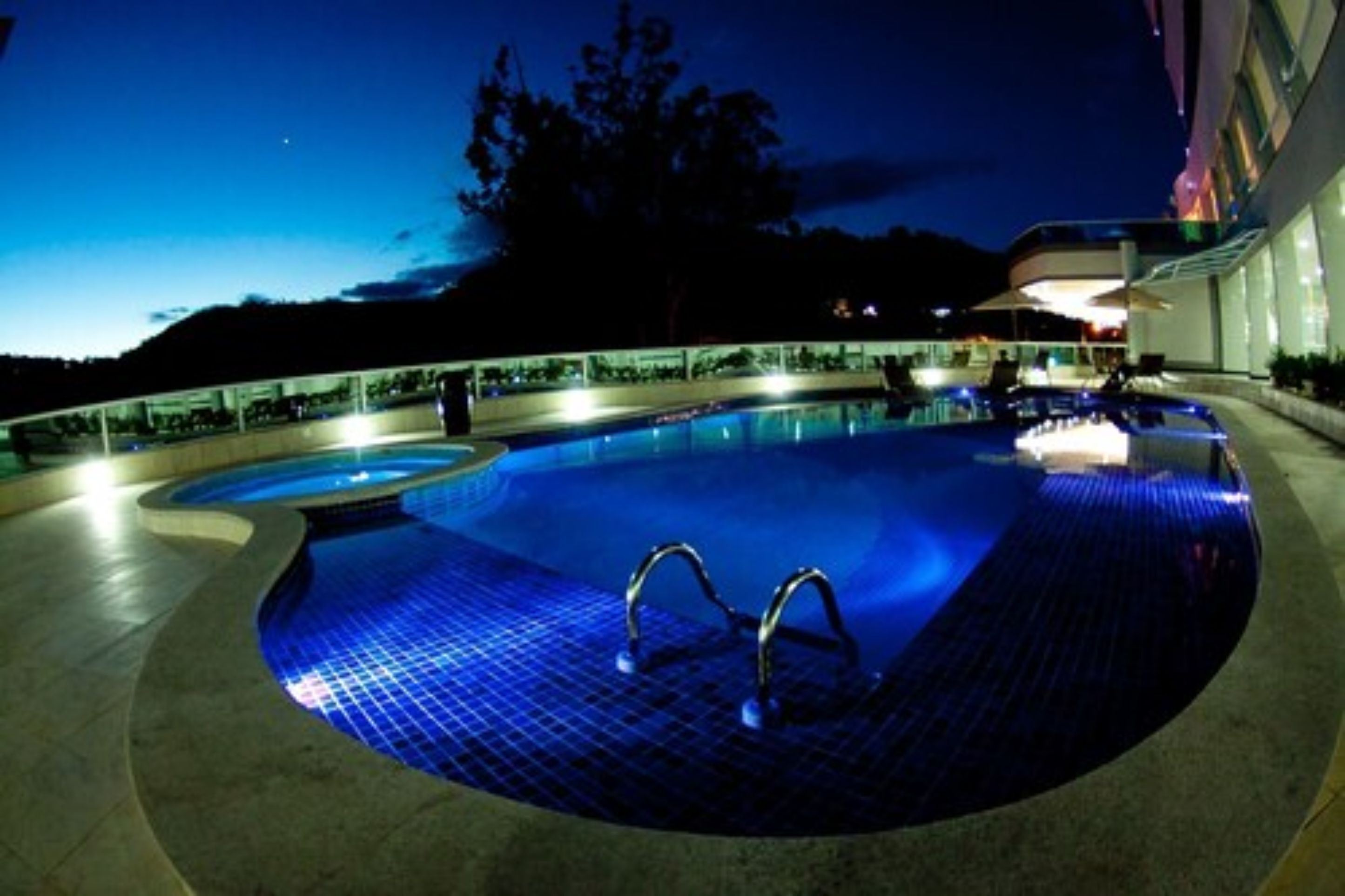 Piscina à noite com deck revestido e corrimãos de metal.