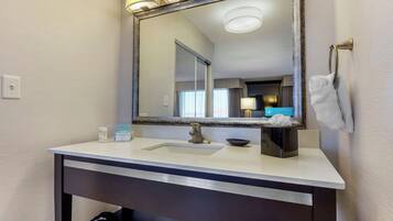 A bathroom with a large mirror, a sink, a towel rack, and a trash bag.