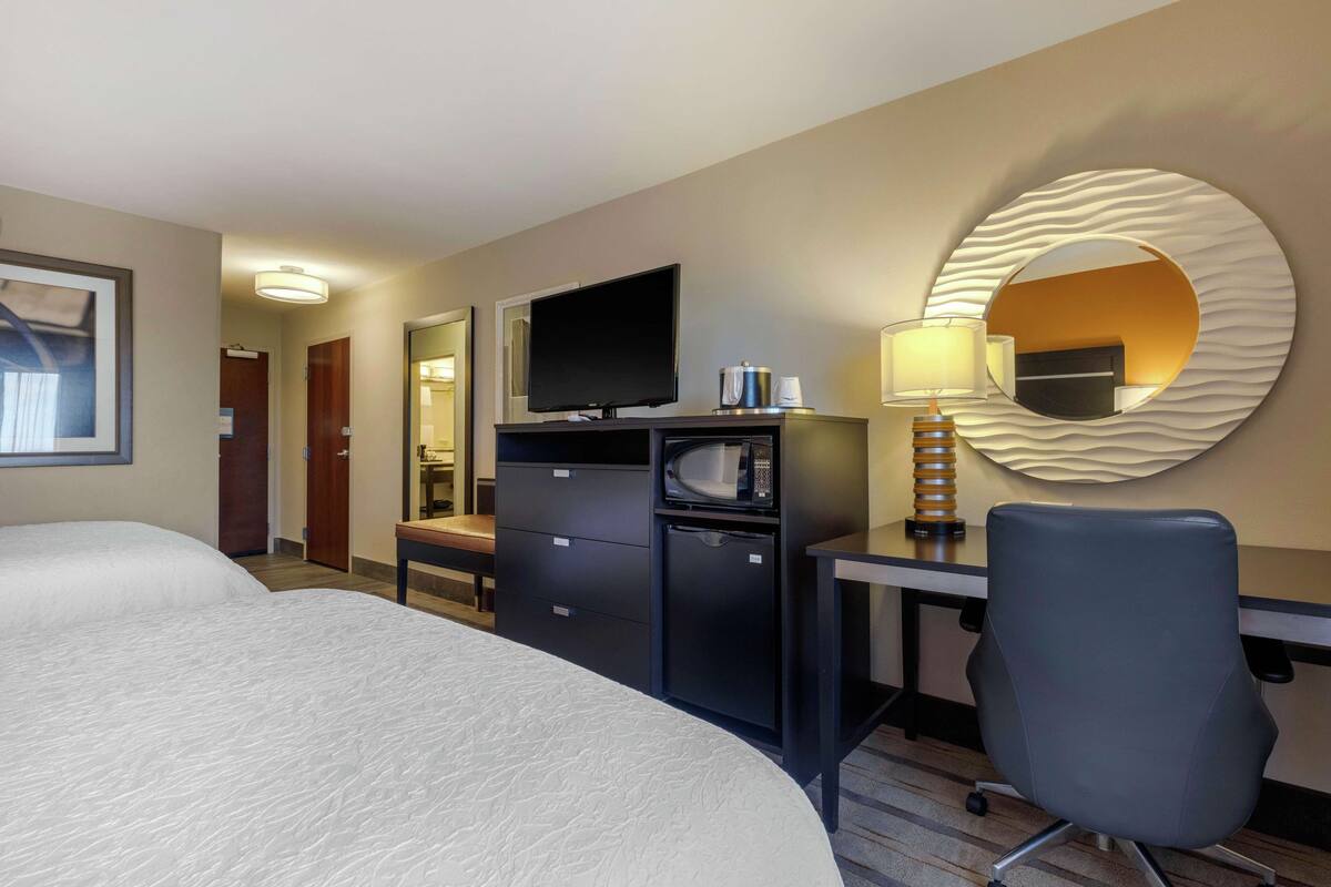 A hotel room with a large bed, a desk with a flat-screen TV, a microwave, a coffee maker, and a modern lamp.