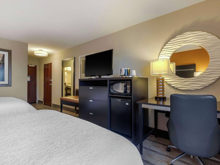 Une chambre d’hôtel dotée d’un grand lit, d’un bureau avec un téléviseur à écran plat, d’un four à micro-ondes, d’une machine à café et d’une lampe moderne.