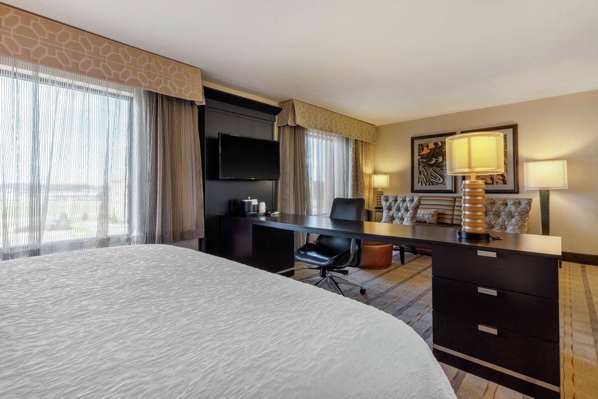 A hotel room with a large bed, a desk with a chair, a television, and a lamp.