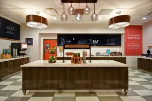 A modern cafe interior with a central island, pendant lighting, and a red accent wall.