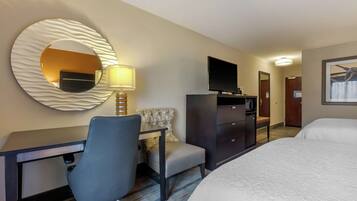 A hotel room with a bed, a desk with a chair, a television, a mirror, and a lamp.