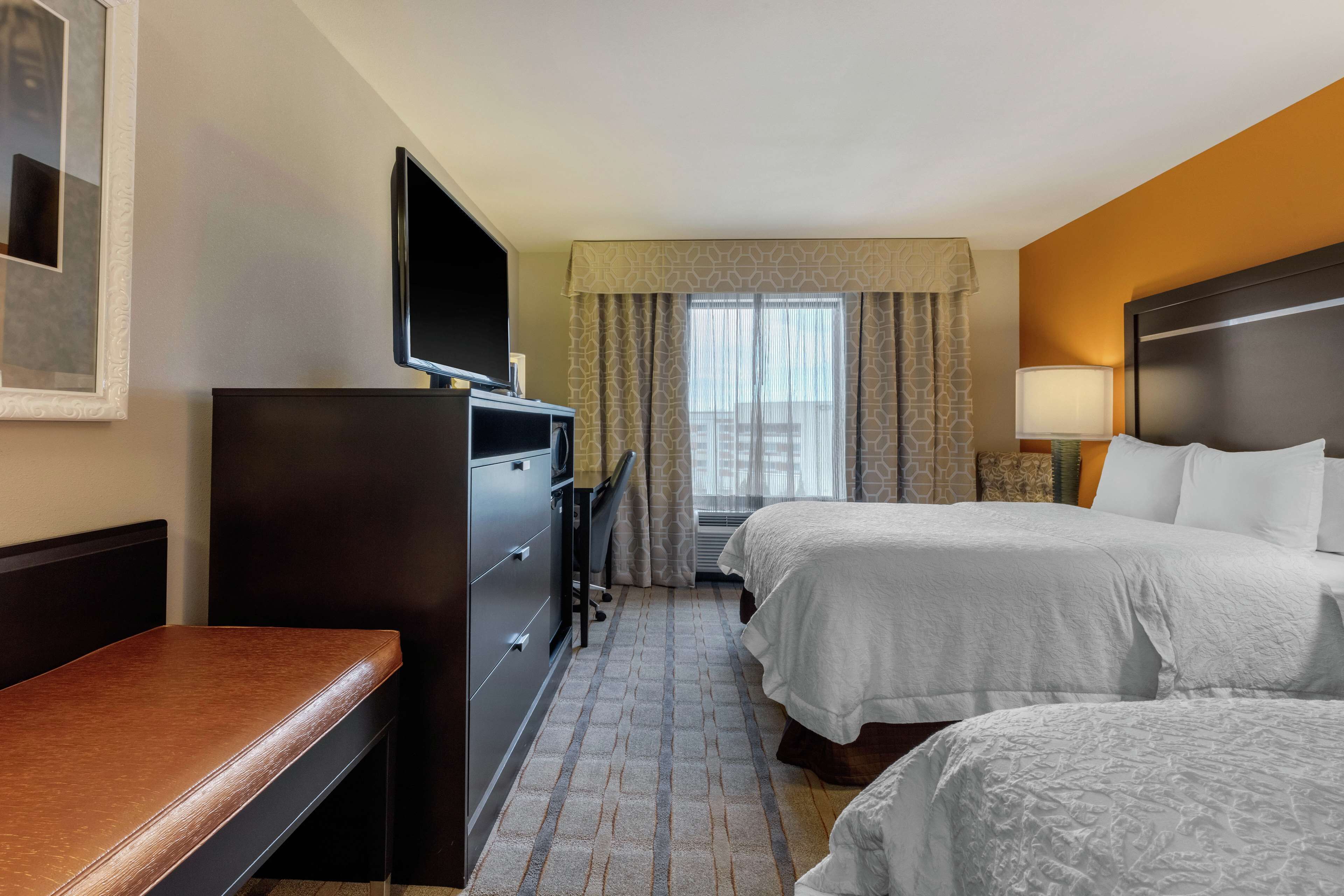 A hotel room with two beds, a desk, a TV, and a window with curtains.