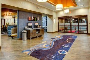A hotel lobby with a reception desk, a bar area, and a seating area with chairs and a patterned rug.