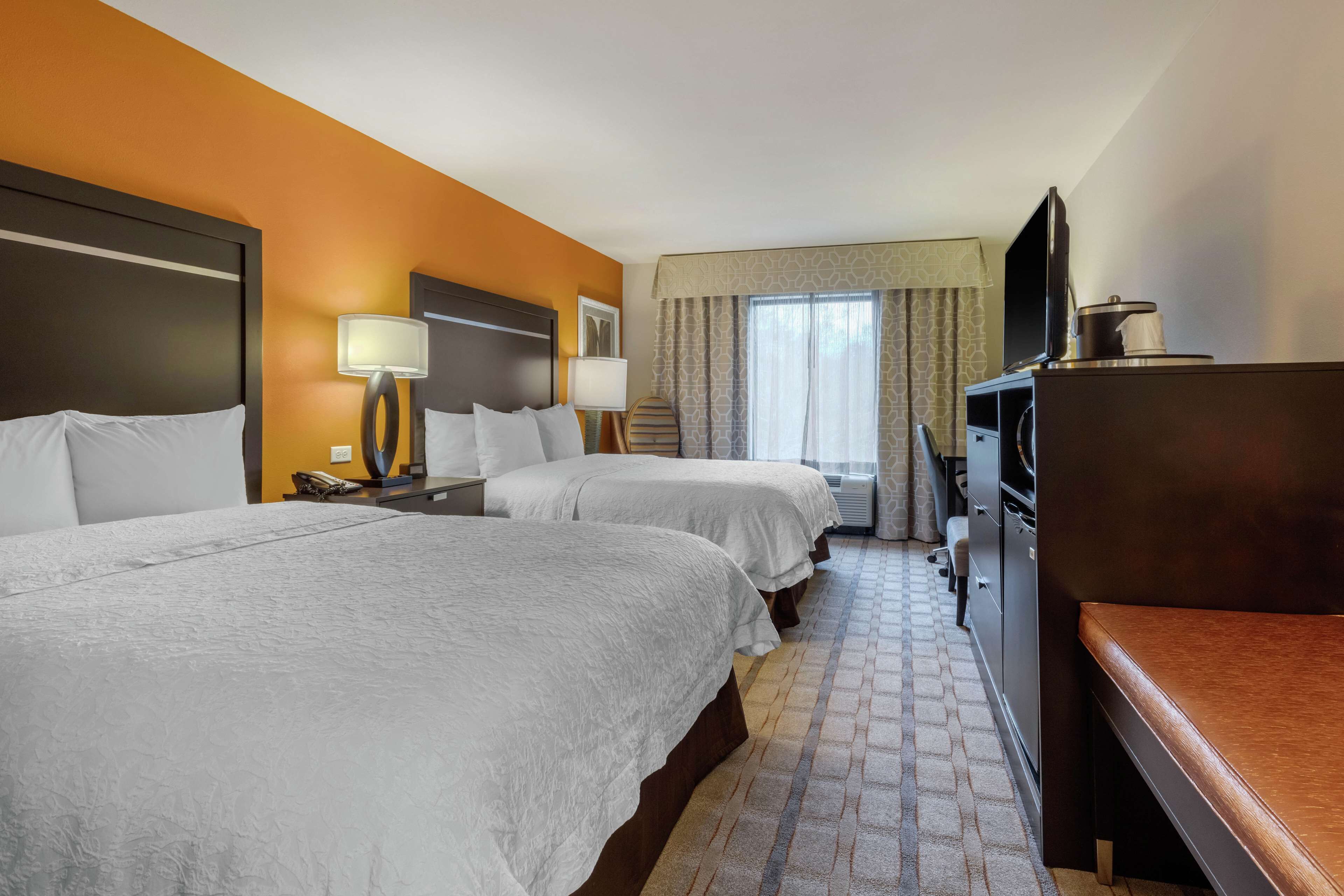 Habitación de hotel con dos camas, un escritorio con televisor, cafetera y ventana con cortinas.