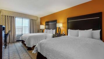 A hotel room with two beds, a desk, a chair, a lamp, and a telephone.