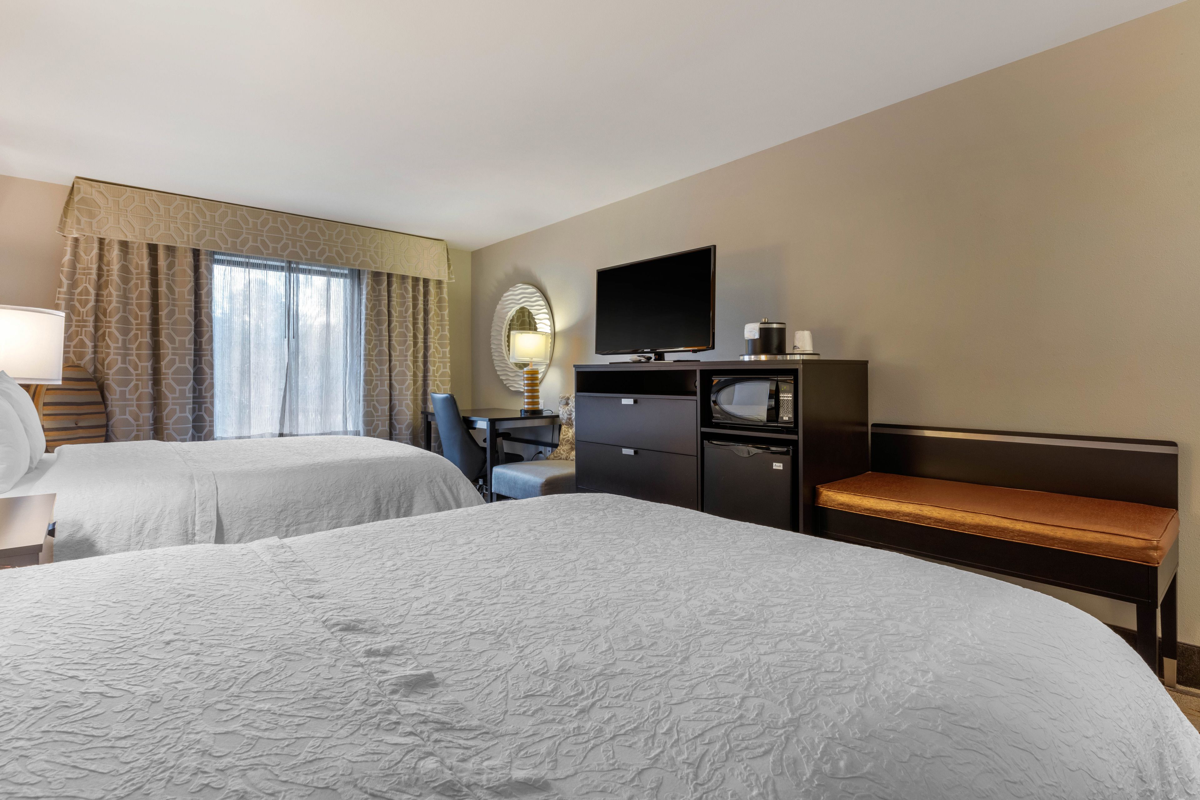 A hotel room with two beds, a desk, a TV, and a minibar.