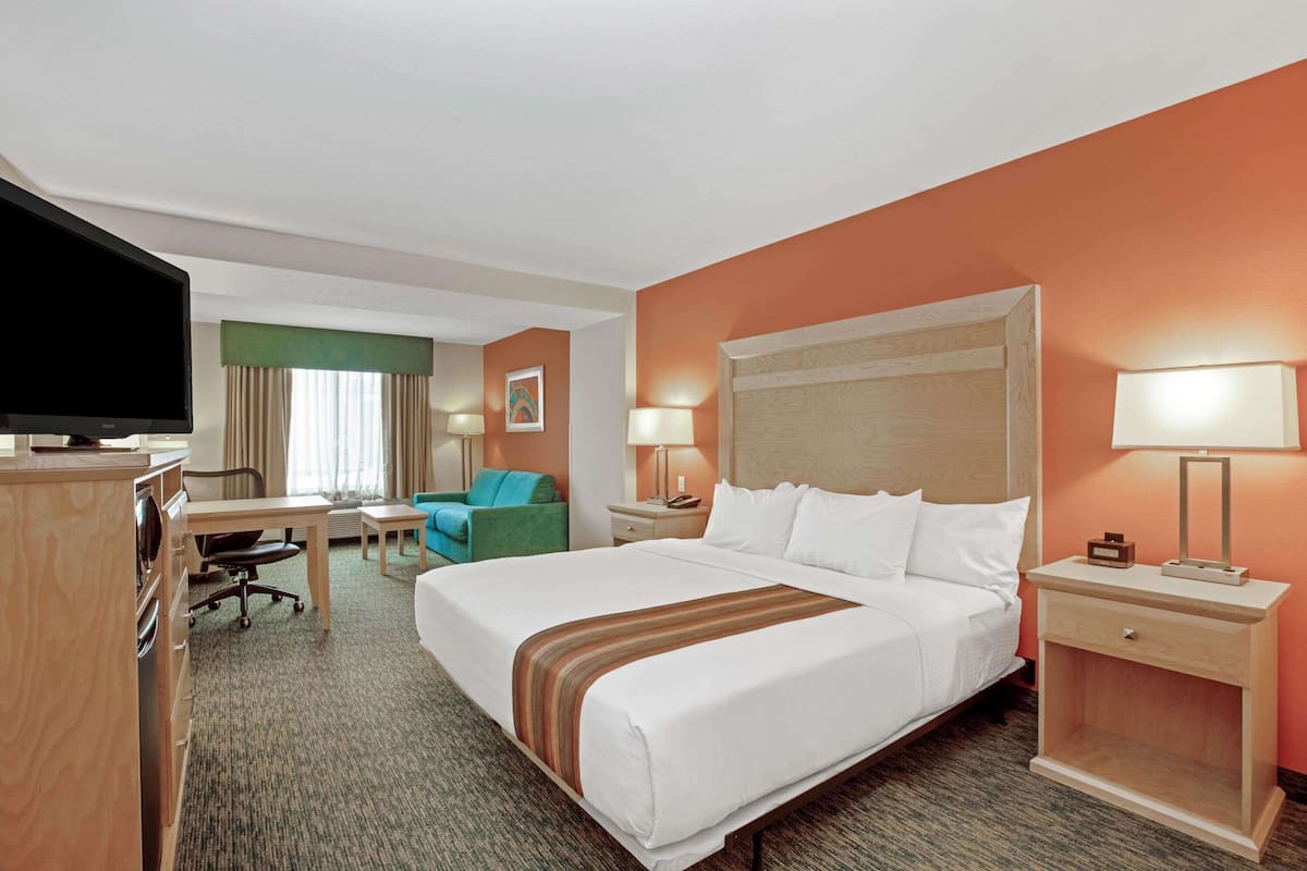 Habitación de hotel con una cama grande, un escritorio con silla, un televisor y una mesita de noche con lámparas.